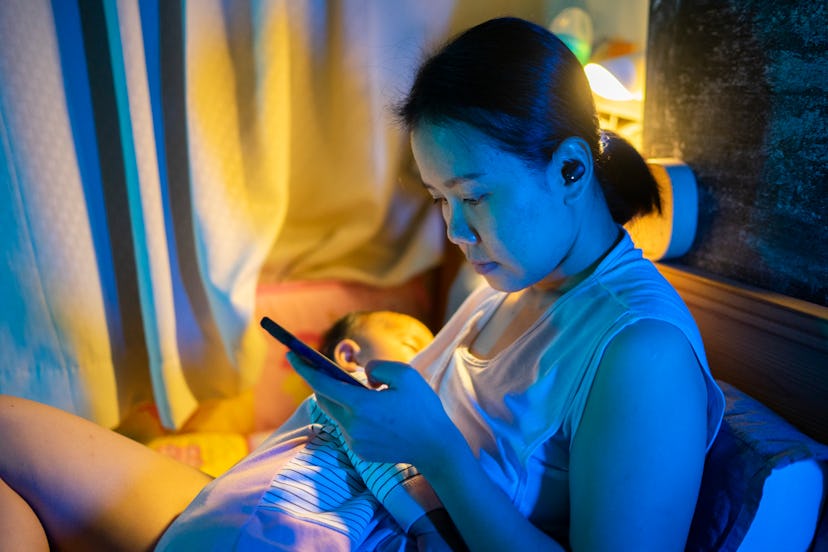 a new mom on her phone in the middle of the night in an article about postpartum insomnia
