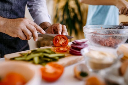 Man cutting pickles and tomatoes on cutting board in the kitchen.