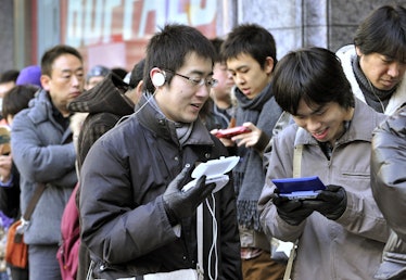 Customers play portable video games as they wait outside an electronics shop to buy the Nintendo 3DS...