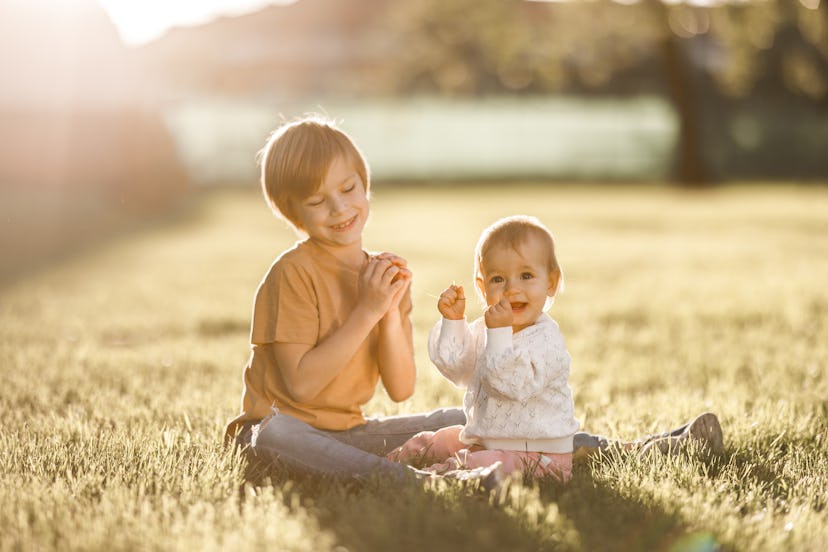 Cute baby girl bonding on the meadow whit her brother during sunny day