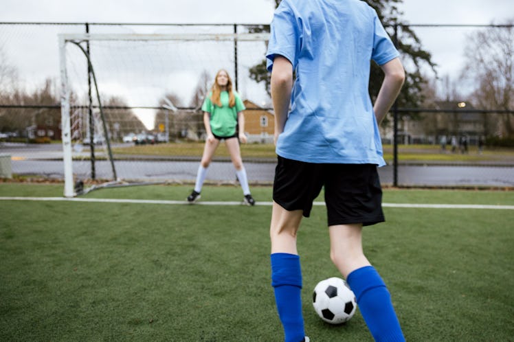 A soccer team practice game consisting of boys and girls on the field. A female goalie defends a go...