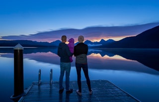 Family take in a vibrant sunrise in the beautiful natural scenery of Glacier National Park's Lake Mc...