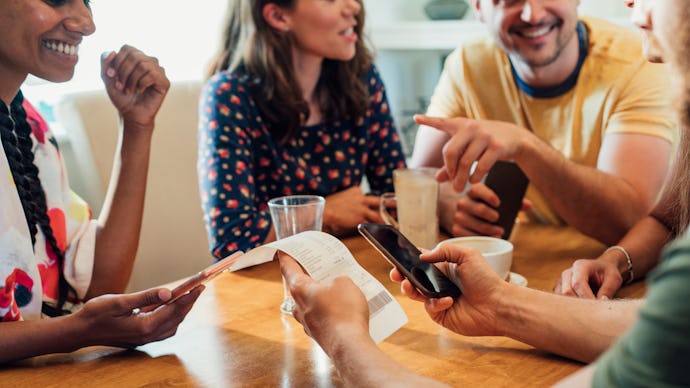 Friend sitting around a table at cafe drinking hot drinks with one person works out their bill with ...