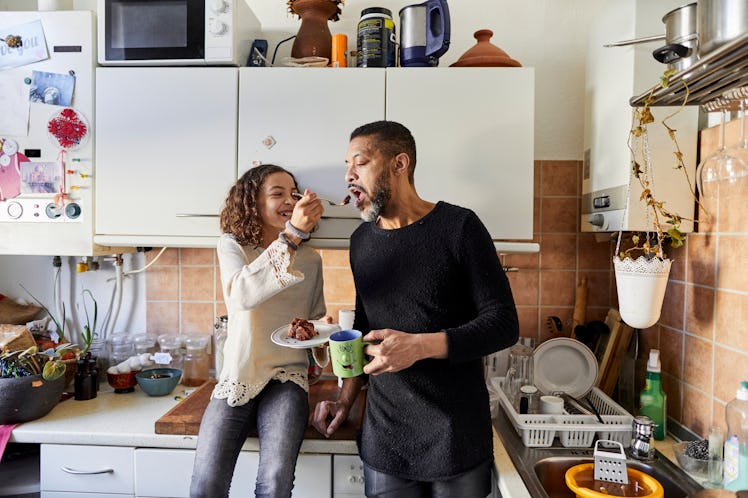 A dad with his daughter in the kitchen as he holds a cup of coffee.