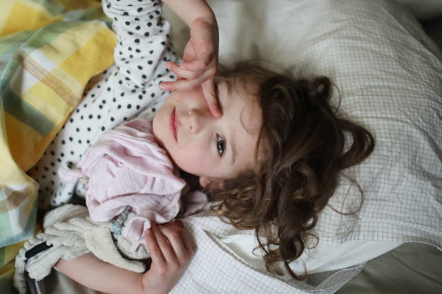 A sick girl rubs her eye while lying in bed. The newest COVID variant may present via itchy eyes or ...