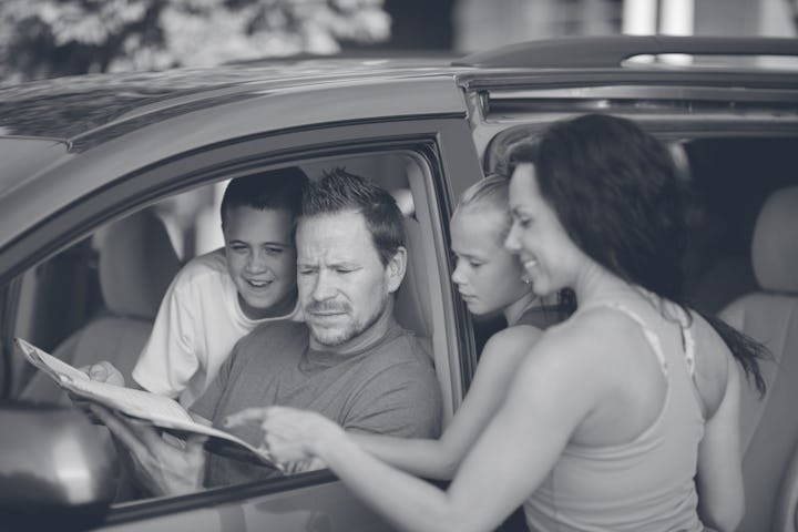 A family of four are getting ready to leave on a road trip and are looking at a map together.