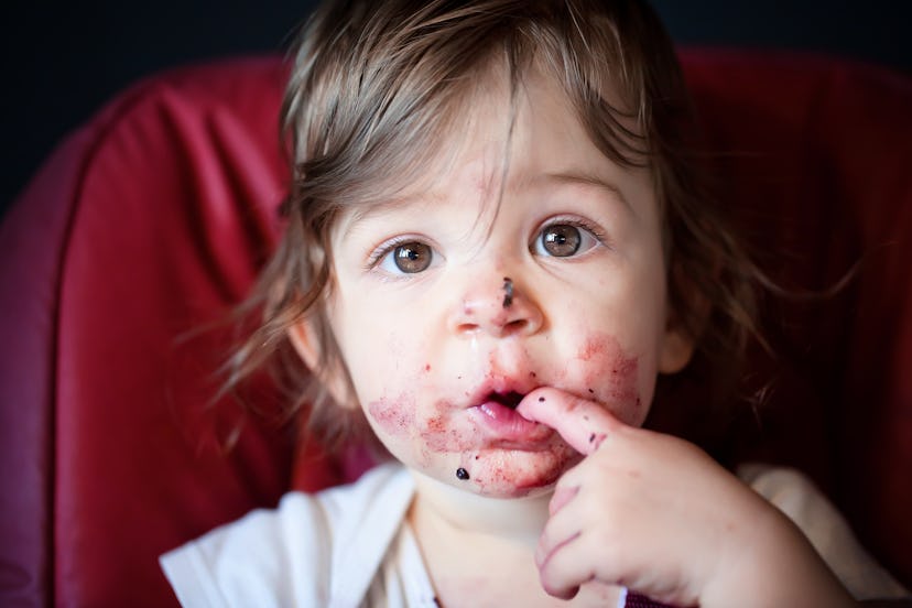Baby girl eating blueberries, finger in her mouth. In an article about when can babies eat baby food...