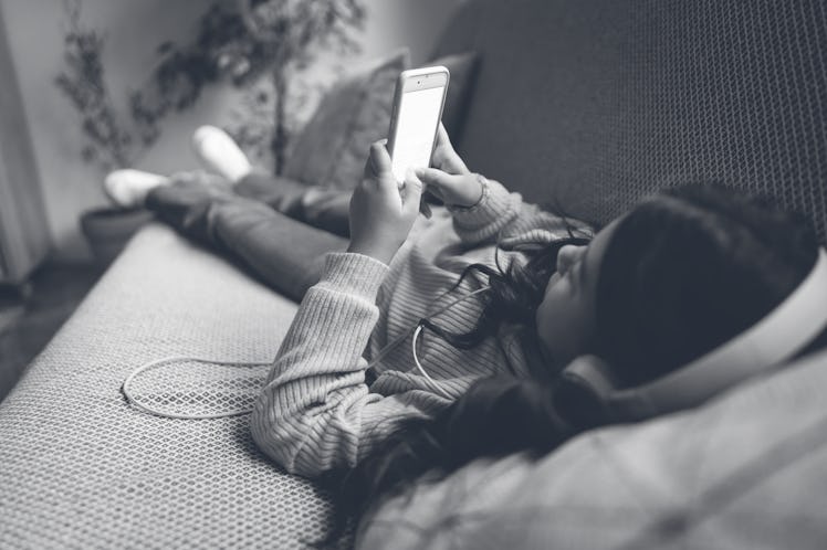 Caucasian schoolgirl lying on the sofa, listen to music while using mobile phone