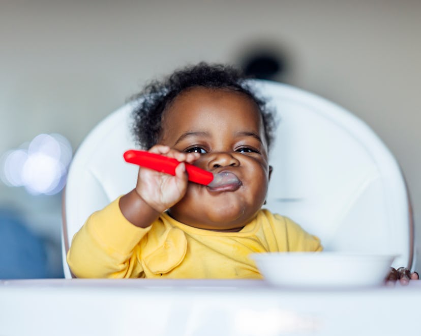 cute baby in a high chair eating food in an article about when can babies eat baby food?