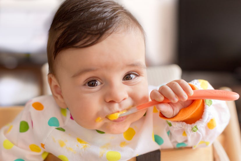 A baby feeds himself a puréed baby food in an article about when can babies eat baby food?