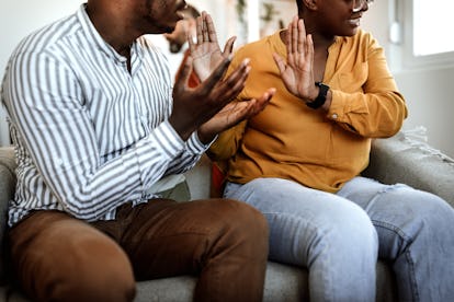 Angry young couple arguing while sitting on couch with marriage counselor in background at office