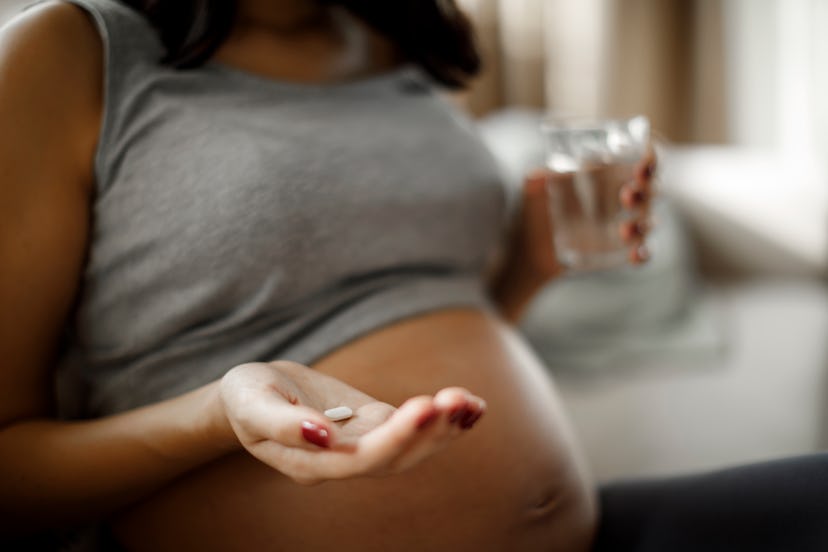 Can you take Tylenol while pregnant? A pregnant person holds up a caplet and a glass of water.