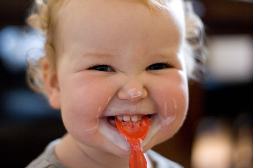 Little girl with plastic spoon in mouth and yoghurt over face. Can babies have yogurt?