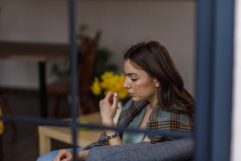 Candid shot of anxious young woman sitting on the sofa in her living room, wrapped in a blanket, wor...