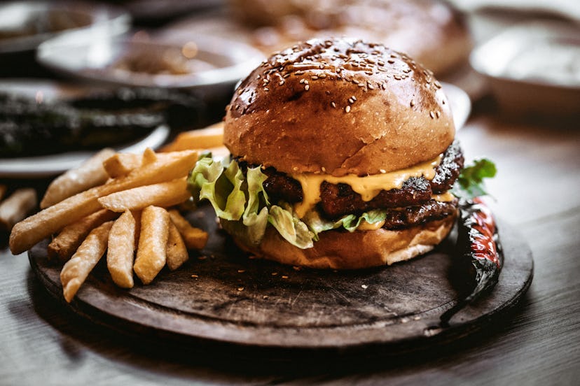 Delicious double burger with french fries and vegetables on wooden cutting board