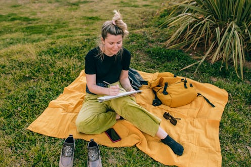 Young beautiful woman drawing on a sketchbook sitting on a blanket in a public park