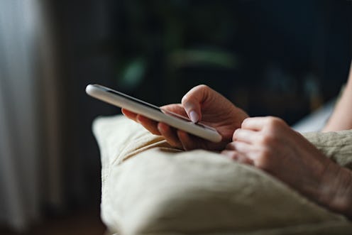 An anonymous woman typing text message on her smartphone while lying on a bed in the morning.