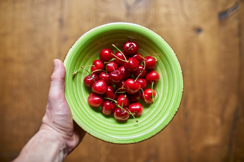 Personal perspective of man holding a green bowl with some cherries
