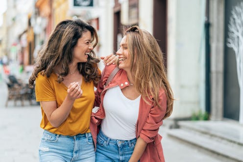 Two young women walking in the city street together. Female friends Smiling, talking and laughing, e...