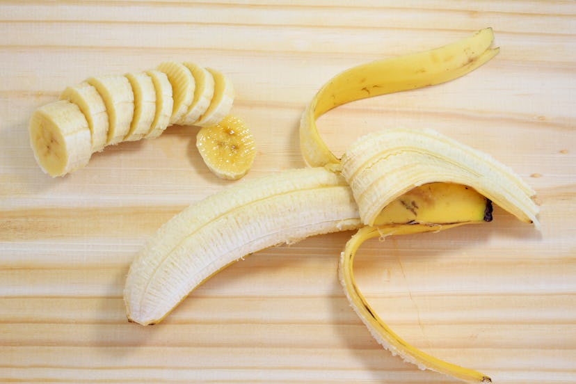 peeled banana on wood next to sliced banana, top view
