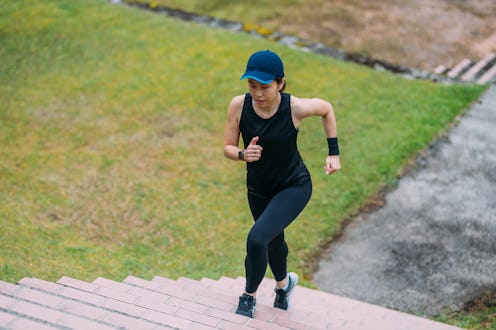 Top view of mature sporty Asian woman running upstairs to public park while training in open air. Sc...