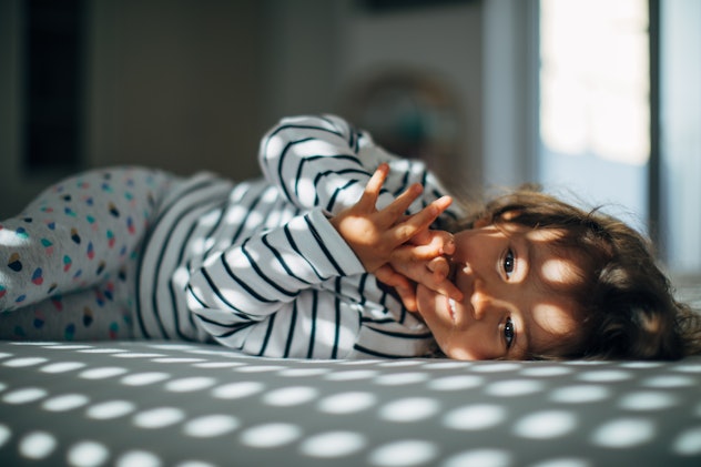One little girl lying in bedroom bed alone on a beautiful morning. What not to do during a sleep reg...