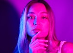 young woman lit by neon pink lights poses for a portrait as she considers how the May 2024 full flow...