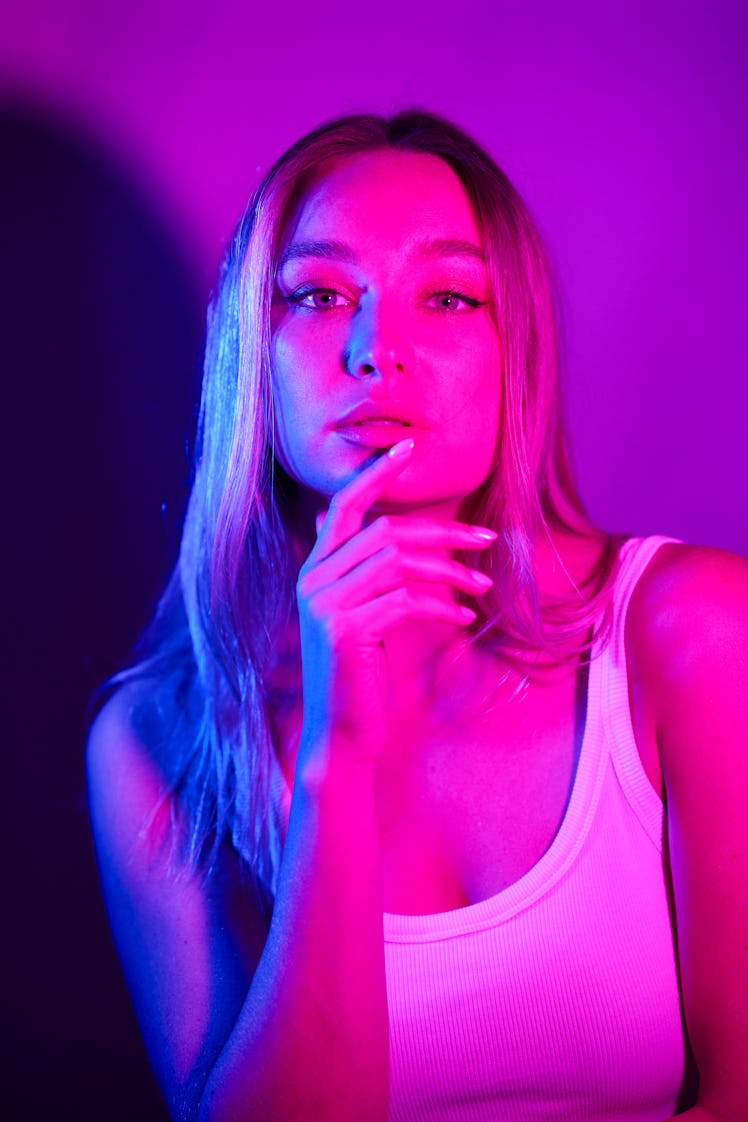 young woman lit by neon pink lights poses for a portrait as she considers how the May 2024 full flow...
