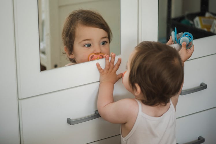 A baby girl is looking herself in the mirror