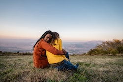 Friends sitting on meadow at sunset embracing. How to support someone who lost a child on mothers da...