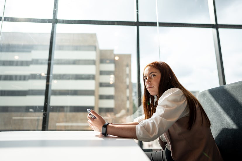 Young woman looking around while using mobile phone at work