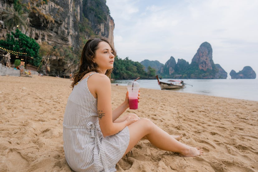 Young Caucasian woman  drinking purple dragon fruit smoothie on the beach