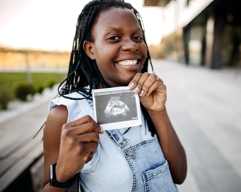 Unrecognizable pregnant woman showing ultrasound of her baby, mother's day pregnancy announcement id...