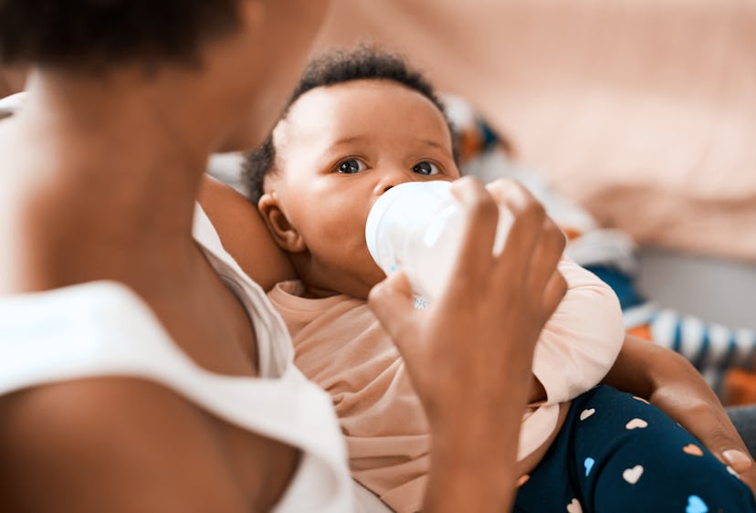 Shot of a black mother feeding her adorable infant daughter at home with bottle in article about com...