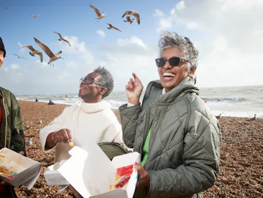 Cheerful male and female friends having french fries at beach on sunny day