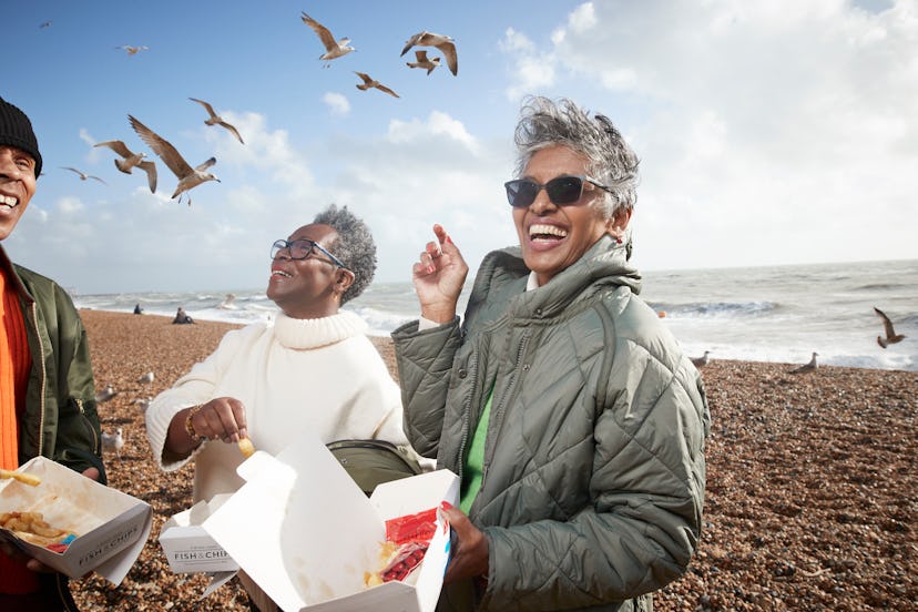 Cheerful male and female friends having french fries at beach on sunny day