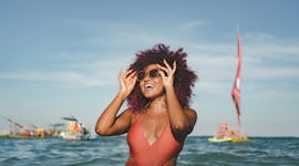 young woman poses in the ocean at the beach with sunglasses as she considers how Mercury Retrograde ...