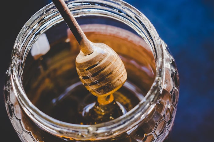 Why can't babies have honey? A honey stir stick drips honey over a full jar.