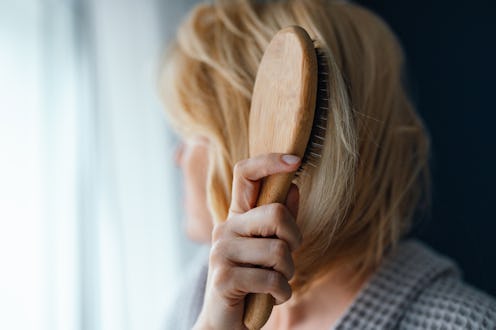 An anonymous woman in bathrobe combing hair while sitting in the bedroom and looking through the win...