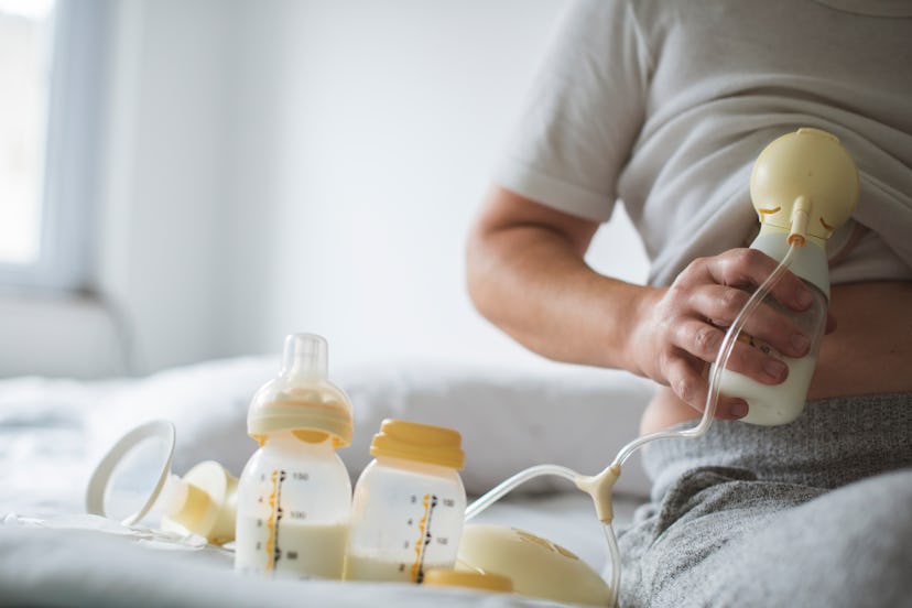 Woman pumping breast milk sitting on edge of bed  in article about how to pump and store breast milk