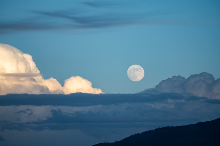 A full moon in the sky, surrounded by clouds.