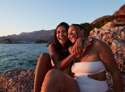 Cheerful young woman sitting on a rock laugh together, as they chat about the three zodiac signs tha...