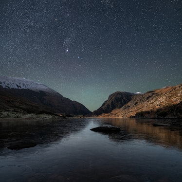 The starry night sky over mountains and water.