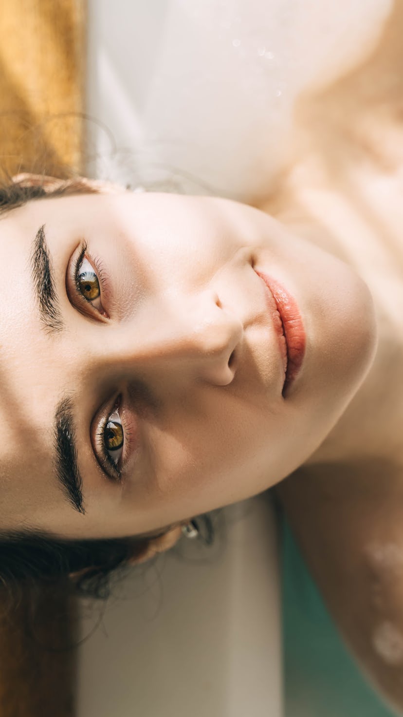 Young woman relaxing in bath tub full of foam bubbles. Self care and mental health concept. Top view...