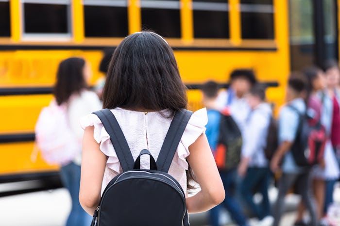 A female middle school student walks hesitantly to the school bus on the first day of school.