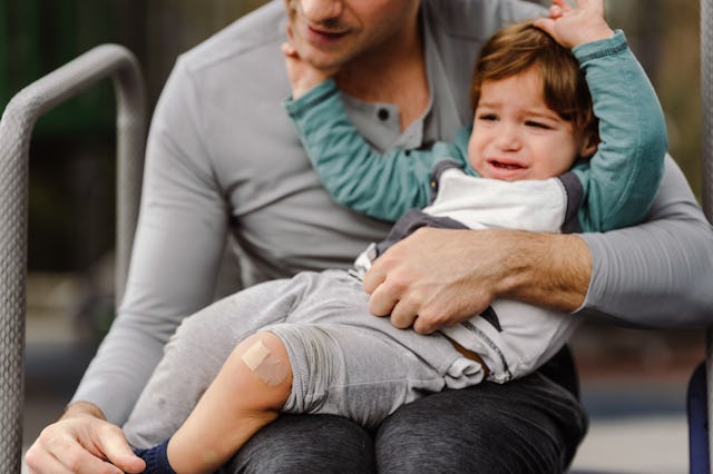 A multiracial one year old boy of Latin American descent sits on his father's lap and cries after hu...