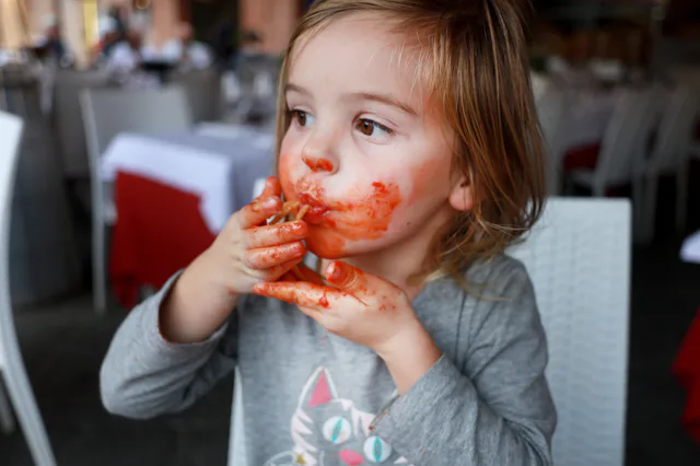 A three year old girl eating home made pasta in a restaurant in The Piazza del Campo in Siena, Ital...
