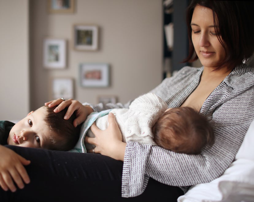 a mom breastfeeding an infant and soothing a toddler. she surely feels a bit touched out.