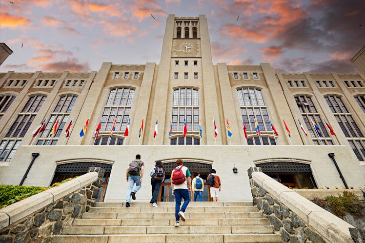 Low angle view of men and women with backpacks walking up staircase to building entrance with dramat...