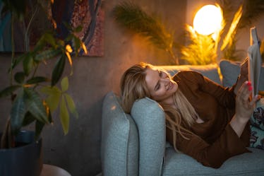 Beautiful young woman relaxing on sofa in living room and reading a book.